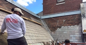 HKC Roofing worker on a commercial slate roof repair project next to a brick building
