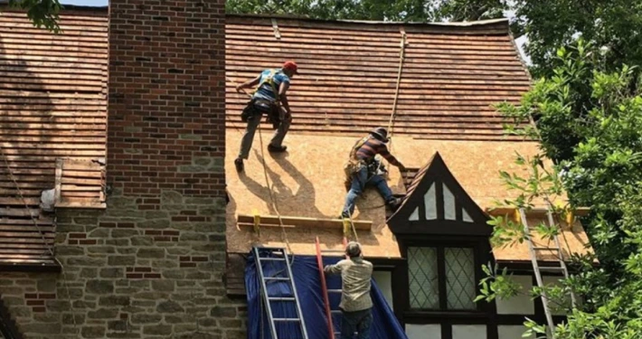Roofing crew performing residential roof repair on a steep Tudor-style brick home in Louisville, KY