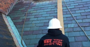 HKC Roofing and Sheet Metal worker in a hard hat inspecting a residential slate roof in Louisville, KY