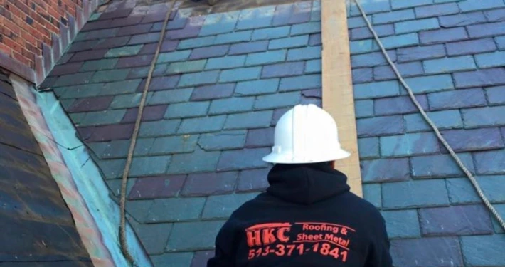 HKC Roofing and Sheet Metal worker in a hard hat inspecting a residential slate roof in Louisville, KY