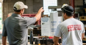 Two HKC Roofing workers reviewing roofing materials and supplies in a warehouse
